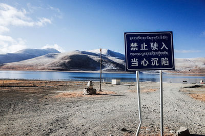 Information sign on road by mountain against sky