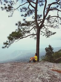 Man sitting on tree by mountain against sky