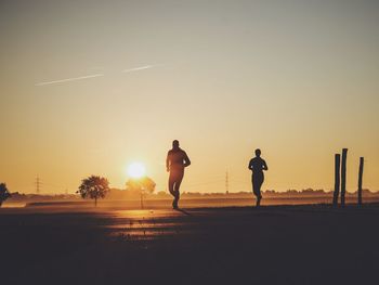 Silhouette people jogging on road against sky during sunset