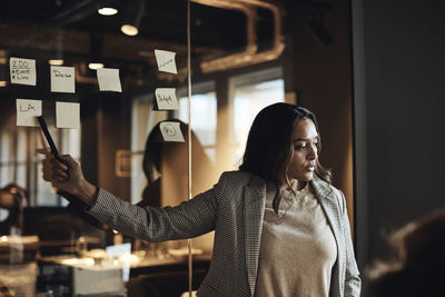 Businesswoman pointing at adhesive note on wall during meeting in office