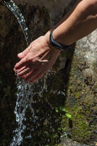 Cropped image of hand by splashing water fountain outdoors