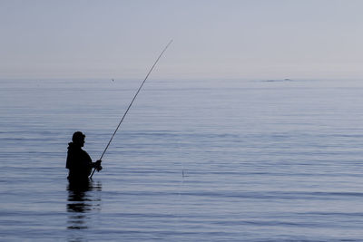 Man fishing in sea against sky