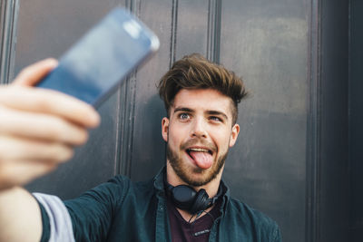 Portrait of young man pulling funny face taking selfie with smartphone