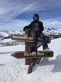 Hiker sitting on information signs on snow covered field against sky