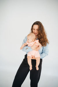 Young mother with long hair and in a shirt holds a newborn daughter. in the arms of a 6 month old 