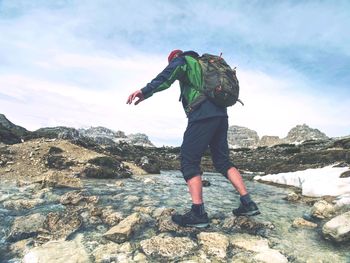 Man with backpack in trekking boots moves over mountain river. hiker wading stream