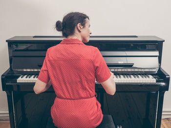 Rear view of woman playing piano at home