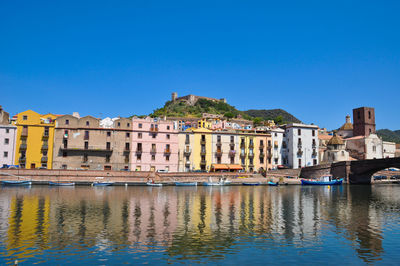 Buildings by river against clear blue sky