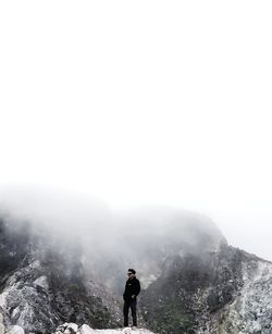 Rear view of man walking on mountain against clear sky