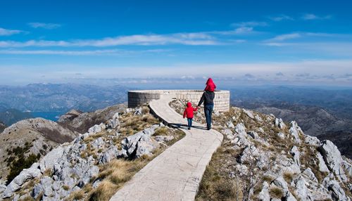 Rear view of father walking with children on mountain against blue sky