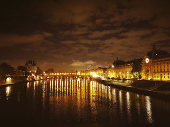 Illuminated city by river against sky at night