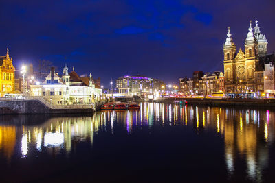 Illuminated buildings by river against sky at night