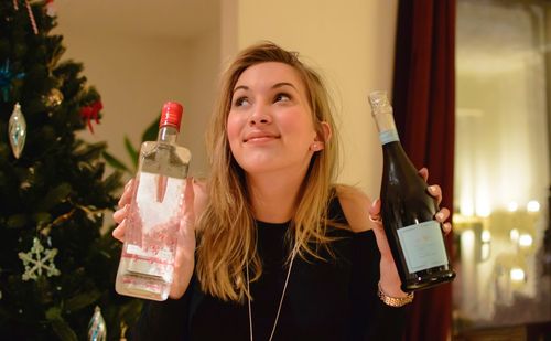 Smiling woman looking away while holding bottles during christmas