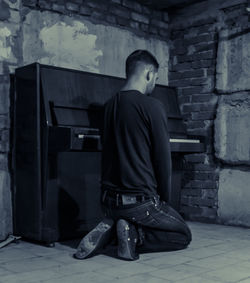 Full length of man kneeling by piano in abandoned room