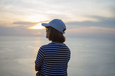 Rear view of woman standing against sea during sunset