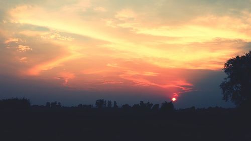 Silhouette trees against dramatic sky during sunset