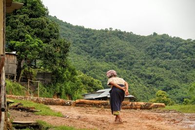 Rear view of senior woman walking on field against green mountain