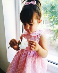 Full length of cute girl holding flowers on window