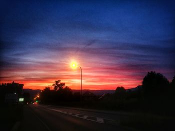 Silhouette trees by road against sky during sunset