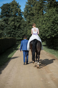 Bridegroom walking by bride riding horse on road