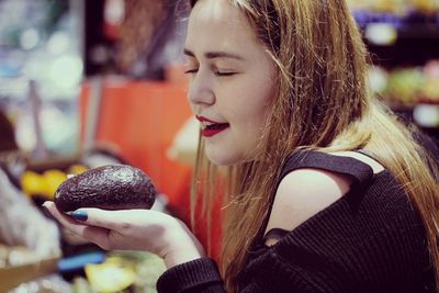 Woman with eyes closed holding avocado at supermarket