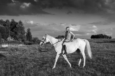 Side view of girl horseback riding on field against sky during sunset