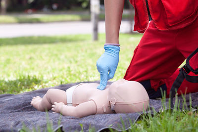 Midsection of person touching baby mannequin lying on grass field