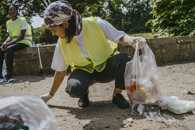 Young female volunteer picking up plastic waste in park