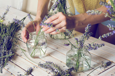 Midsection of florist arranging lavender flowers in jar on table