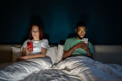 Young multiracial couple lying in bed using smartphones not talking