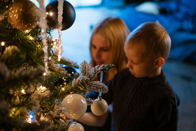 Happy family of two, mother and son decorate the christmas tree.