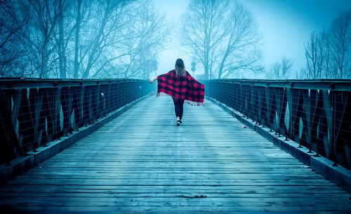 Rear view of woman walking on bridge against sky during foggy weather