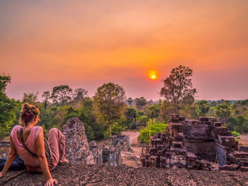 Woman sitting on land against sky during sunset