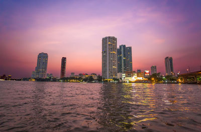 Illuminated modern buildings in city against sky during sunset