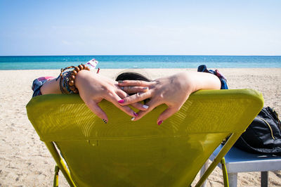 Woman with head behind head sitting on chair at beach against sky