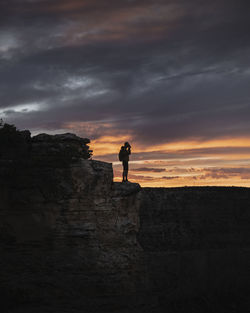 Silhouette man standing on rock against sky during sunset