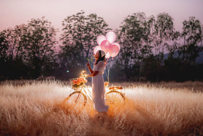 Woman standing on field by trees against sky during sunset