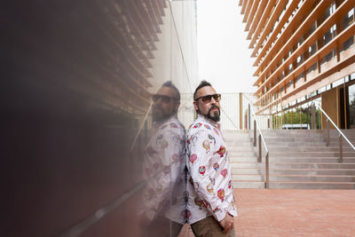 Side view of a bearded male leaning on a office building wall