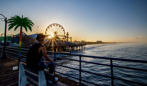 Woman sitting at amusement park by sea against sky during sunset