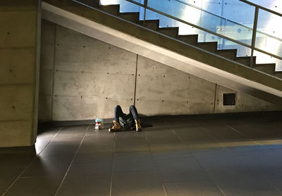 Homeless man sleeping on floor below staircase in building