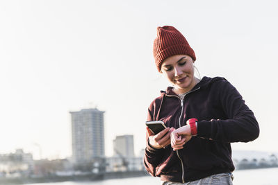 Sportive young woman at the riverside in the city with smartphone and smartwatch