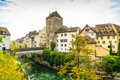 Arch bridge over river amidst buildings against sky