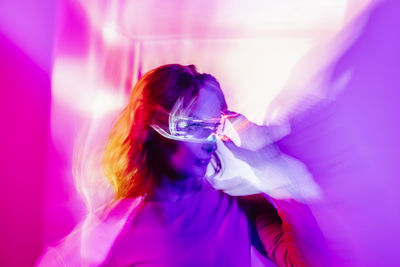 Young woman with long hair and bright makeup looking away in studio with colorful neon illumination