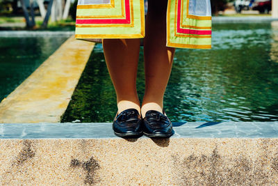 Low section of woman standing on retaining wall by pond