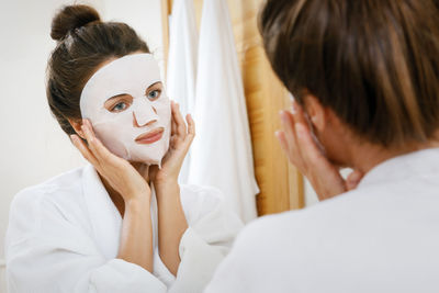 Woman applying sheet mask at home