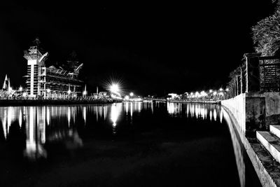 Illuminated buildings by river against sky at night