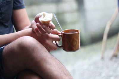 Midsection of man holding coffee cup while sitting outdoors