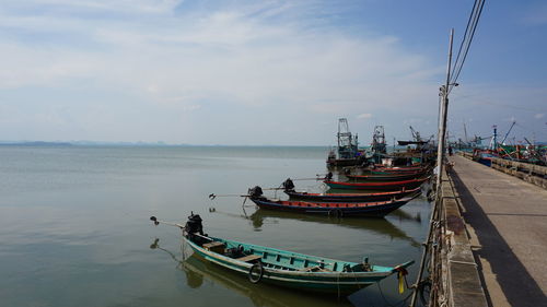 Fishing boats moored at harbor against sky