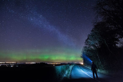 Rear view of man with illuminated headlamp on road against star field