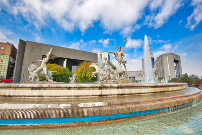 Fountain by swimming pool in city against sky